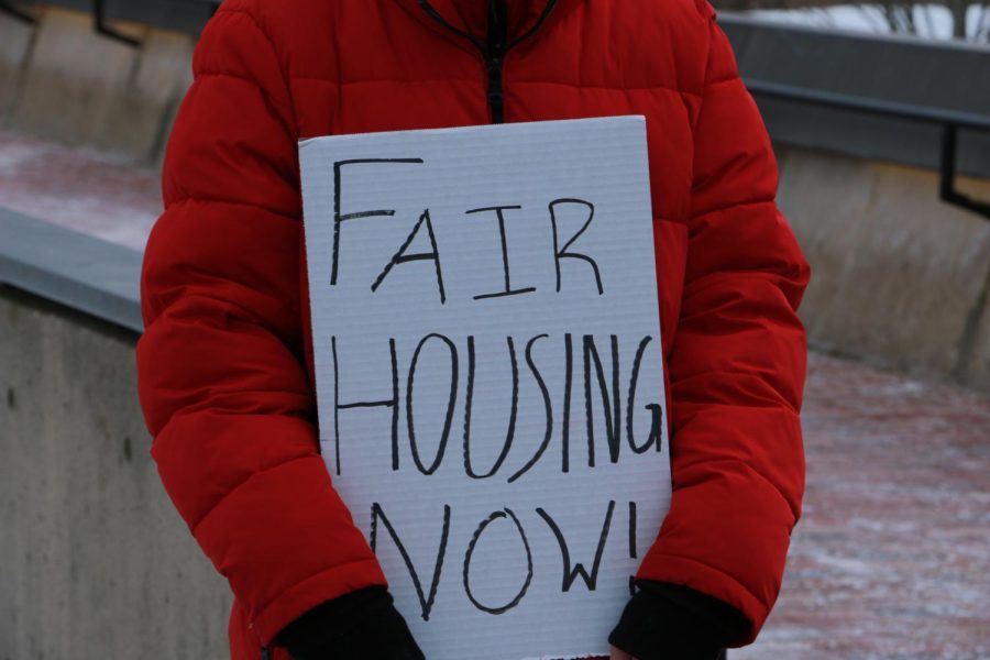 A student protester holds a sign with the phrase fair housing now!